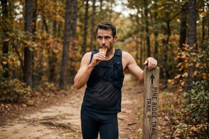 Coureur de trail consommant un gel énergétique à base de miel sur un sentier forestier en automne