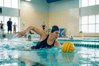 Femme pratiquant le water-polo en piscine intérieure, expression concentrée, éclaboussures autour d'elle, sport aquatique dynamique