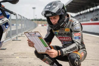 Pilote de moto étudiant le calendrier des courses FFCC pour la saison 2026 dans le paddock d'un circuit