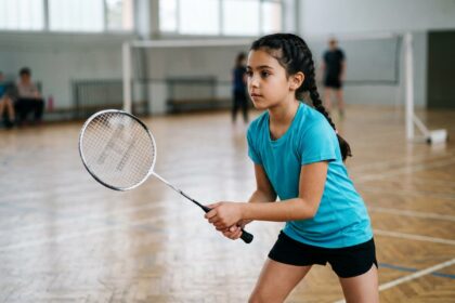 Jeune fille tenant une raquette de badminton junior en salle de sport, idéale pour choisir une raquette adaptée aux enfants